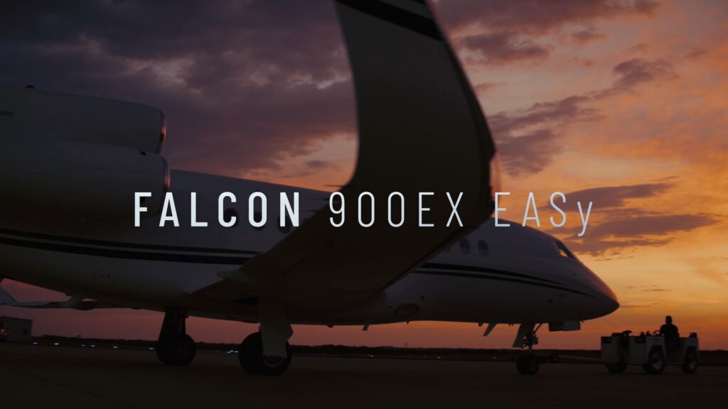 Falcon 900EX EASy jet on the ramp at sunset with a winglet in the foreground and a tug near the nose, with "Falcon 900EX EASy" title text.